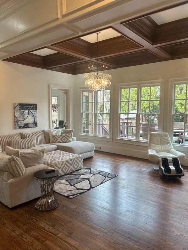 A spacious living room with a large sectional sofa, a massage chair, and a chandelier. - Private Buckhead Estate Pool, Game Room, Custom Kitchen (Atlanta)