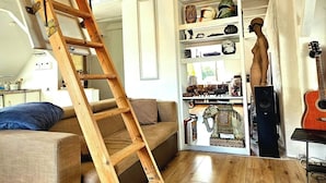 Une pièce de style loft avec une échelle en bois, un canapé, une bibliothèque et une guitare.