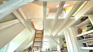 Une pièce de style « loft », avec des poutres en bois apparentes, une échelle en bois et une lucarne.