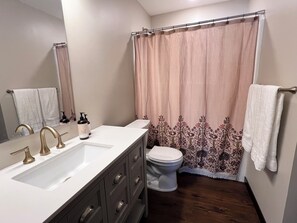 Ein Badezimmer mit einem weißen Waschbecken, zwei goldenen Wasserhähnen, einer Toilette und einem Duschvorhang mit einem Blumenmuster.