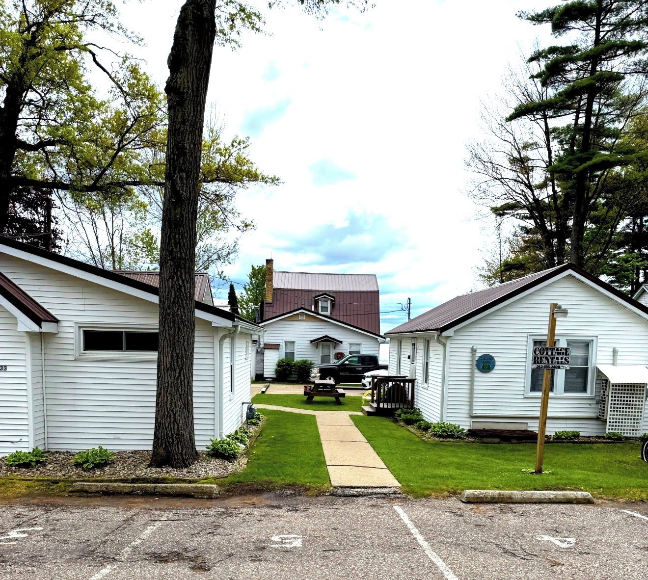 A row of single-story cabins with a central building, a picnic table, and a sign indicating cottage rentals.