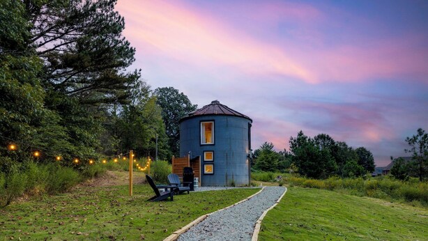 A blue cylindrical building with a door and windows, surrounded by a gravel path and greenery.