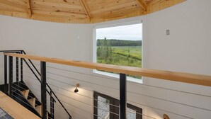 A modern interior with a wooden ceiling, a staircase with black railings, and a large window offering a view of a green landscape.