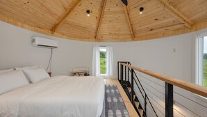 A bedroom with a large bed, wooden ceiling, and a view of greenery outside.