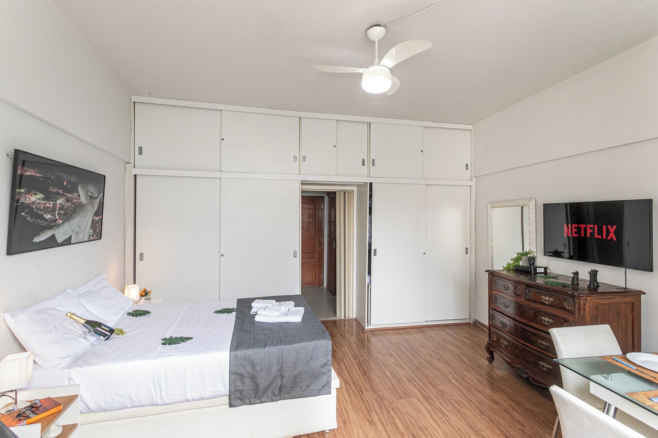 Une chambre d’hôtel équipée d’un lit, d’un bureau, d’une armoire, d’une télévision et d’un ventilateur de plafond.