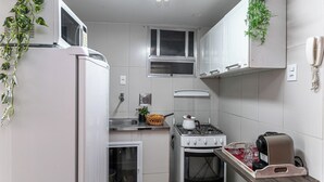 A compact kitchen with white cabinets, a gas stove, a microwave, and a small window. - Incredible view of Cristo Redentor (Rio de Janeiro)