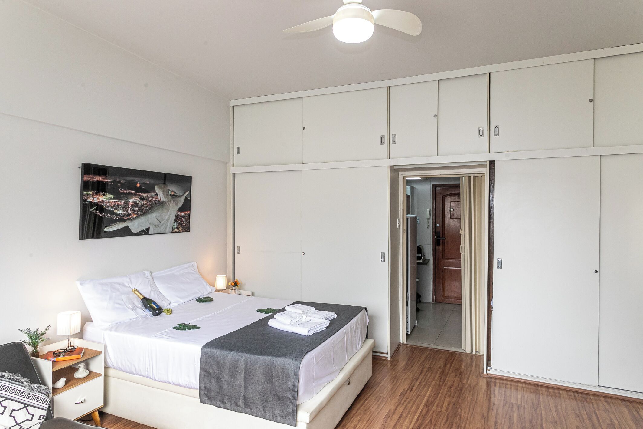 A bedroom with a bed, white wardrobe, and a cityscape painting.