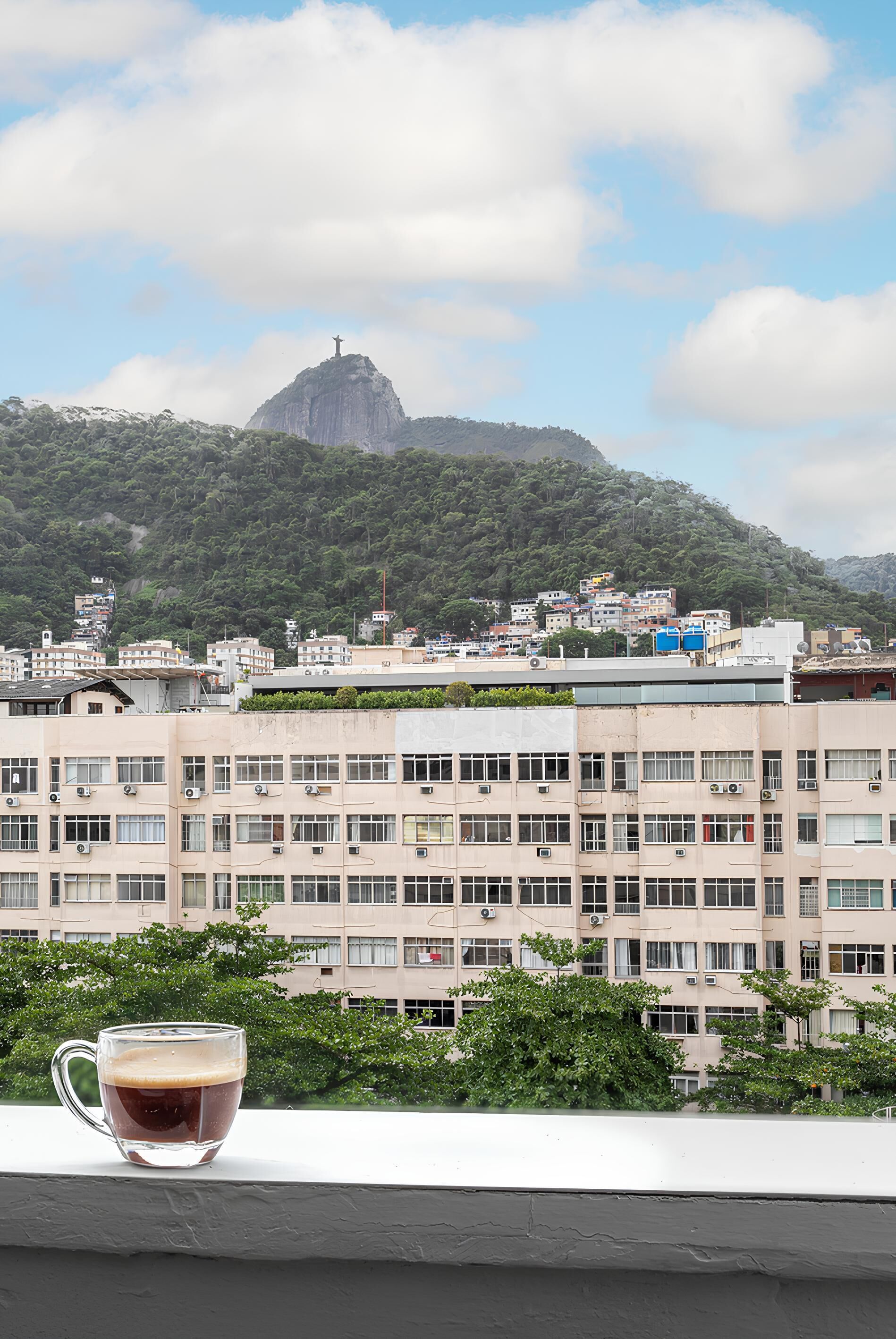 Un edificio con varias ventanas y balcones, cielo despejado y una montaña distante con una estatua.