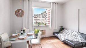 A modern living room with a glass dining table, white chairs, a black sofa, and a view of a cityscape through a large window. - Incredible view of Cristo Redentor (Rio de Janeiro)