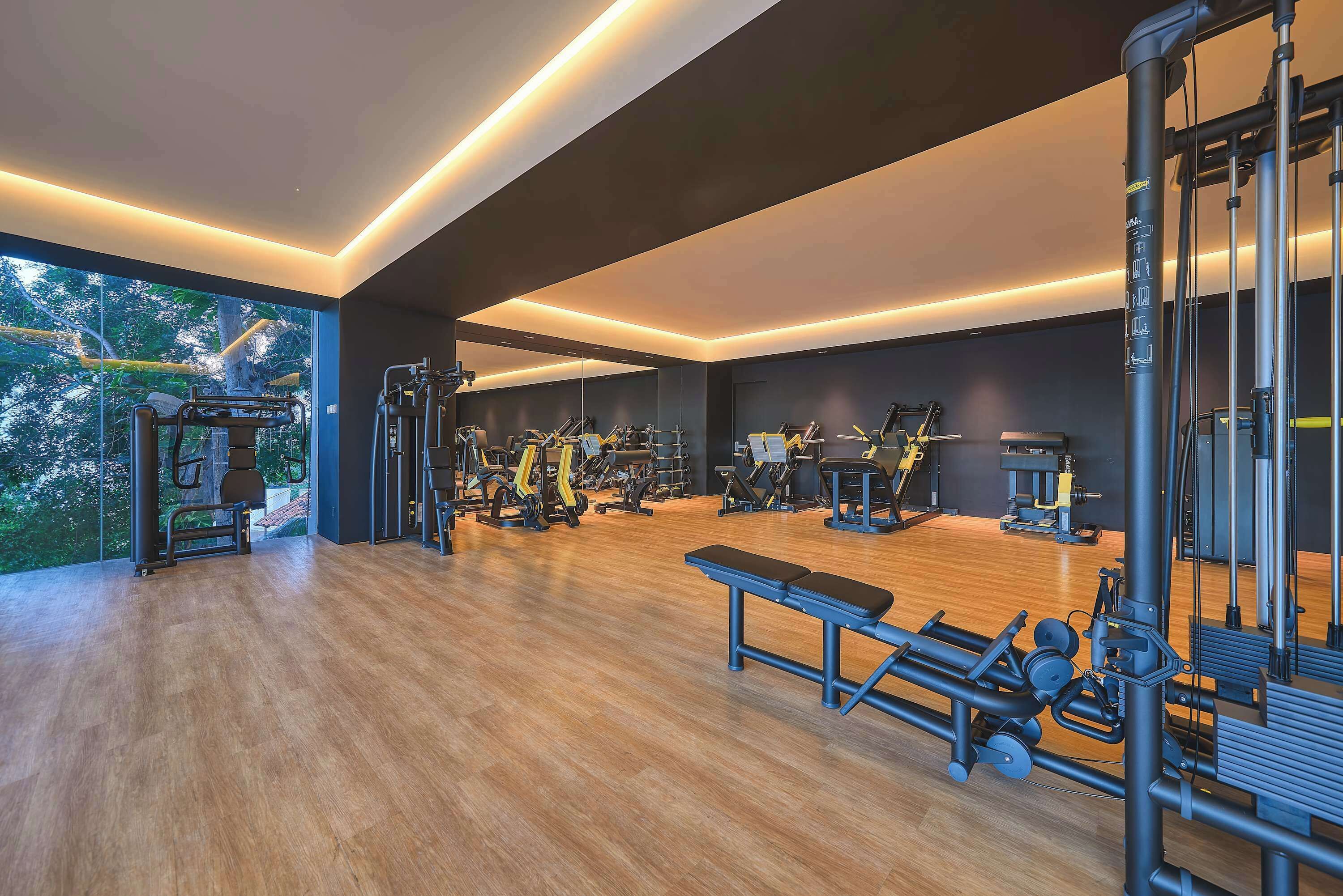 Een moderne sportschool met diverse fitnessapparaten, grote ramen en een houten vloer.