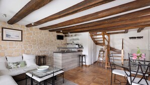 Una sala de estar acogedora con pared de piedra, vigas de madera, una mesa de vidrio y una cocina al fondo.
