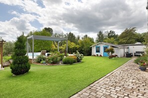 Un patio trasero cuidado con una pérgola, una casita con detalles azules y un camino de ladrillo.