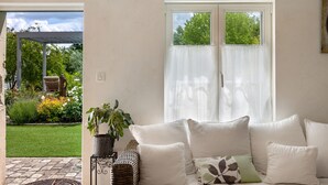 Una habitación con un sofá blanco, una planta en maceta y vista a un jardín a través de una ventana.