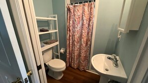 Une salle de bain avec des toilettes, un lavabo blanc, un rideau de douche et une étagère contenant des articles de toilette.