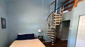 Une chambre à coucher comprenant un lit, une table de chevet, une lampe et un escalier en colimaçon menant à un niveau supérieur.