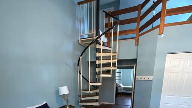 Une chambre à coucher comprenant un lit, une table de chevet, une lampe, un escalier en colimaçon et une armoire.