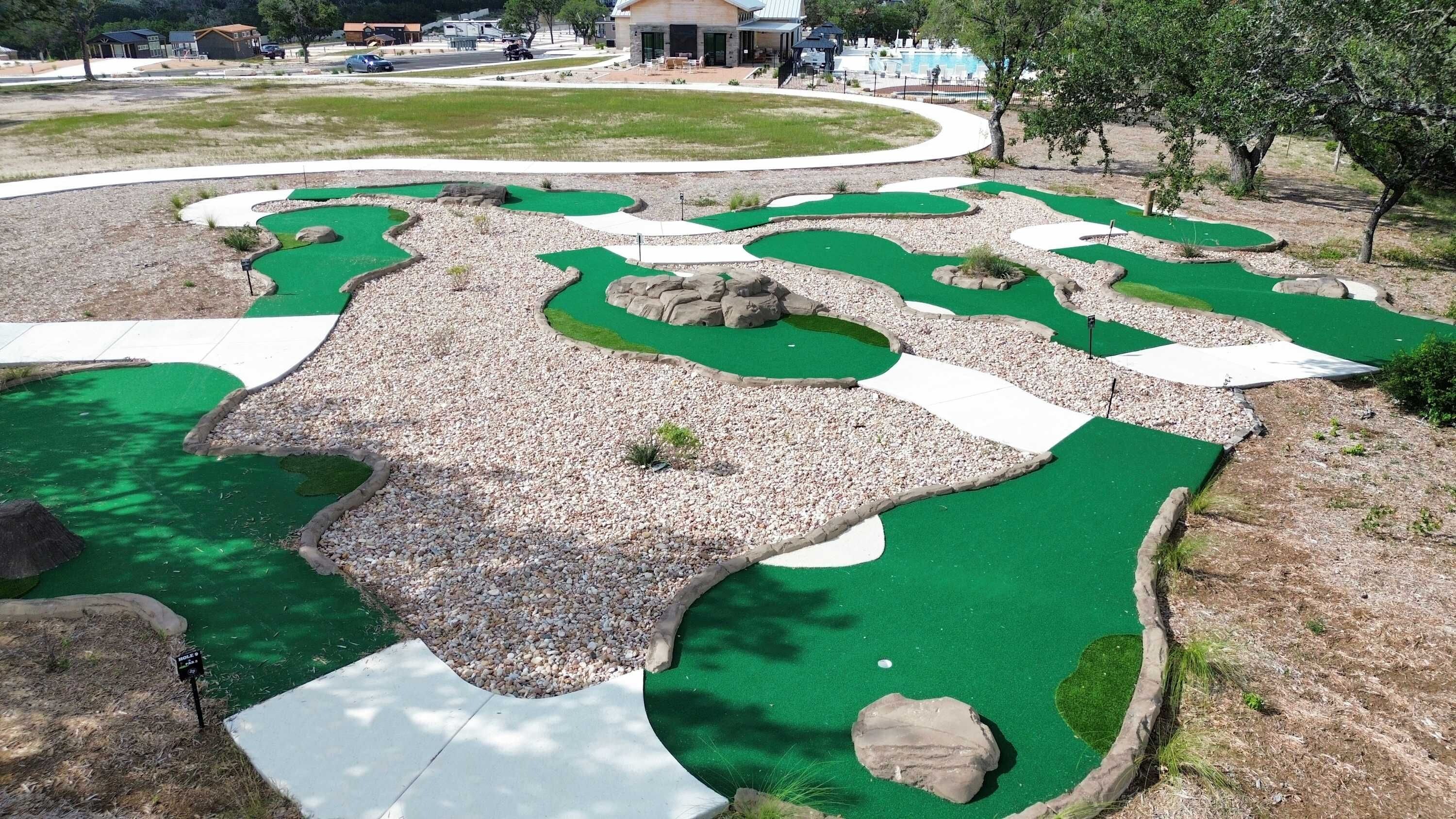 Een minigolfbaan met een slingerend parcours, groene speeloppervlakken en omliggende grindpaden.