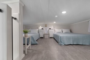 Ein kleines, helles Schlafzimmer mit zwei Betten, einem Nachttisch mit Pflanze und einem kleinen Schrank.