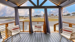 Un espacio al aire libre cubierto con dos sillones de mimbre y un banco, con vistas a un amplio espacio abierto con edificios y una valla.