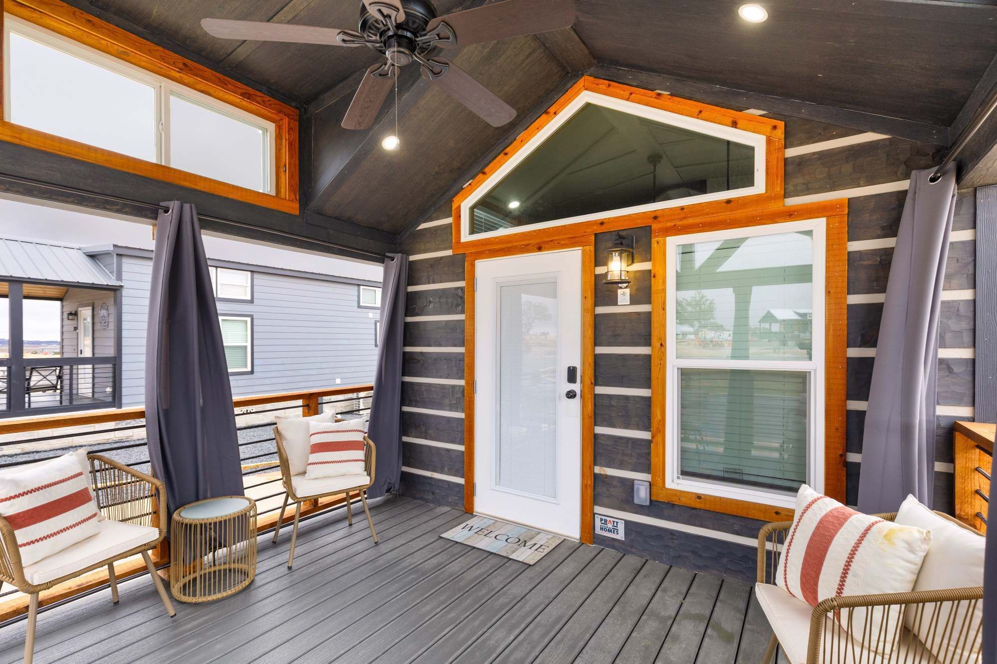 Un porche cubierto con muebles de mimbre, ventilador de techo y vistas al exterior.