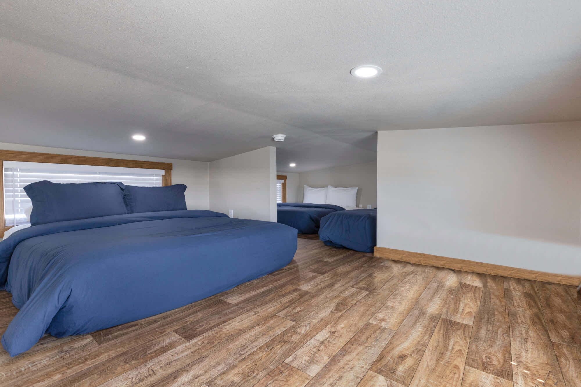 A bedroom with two beds, wooden flooring, and a window with blinds.