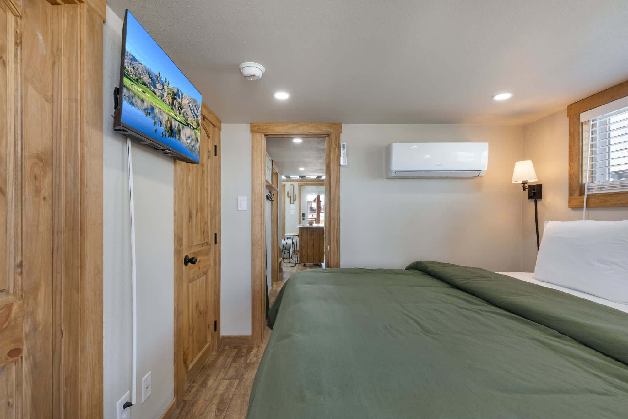 Ein Schlafzimmer mit einem Bett, einem an der Wand befestigten Fernseher, einer Klimaanlage und einem Flur, der zu einem Badezimmer führt.