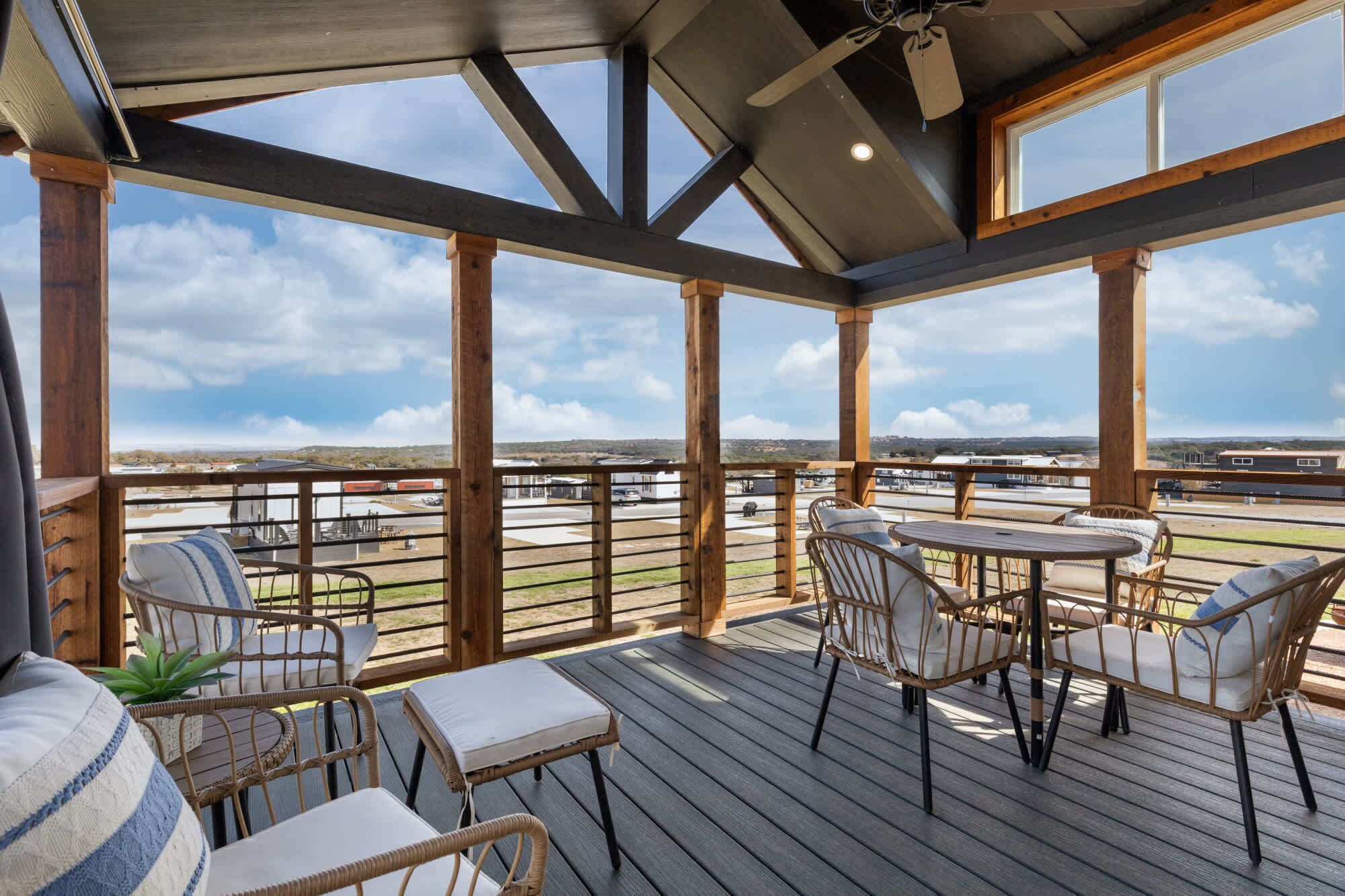 Eine überdachte Terrasse im Freien mit Holzmöbeln und Blick auf die Umgebung, der Himmel ist wolkenlos.