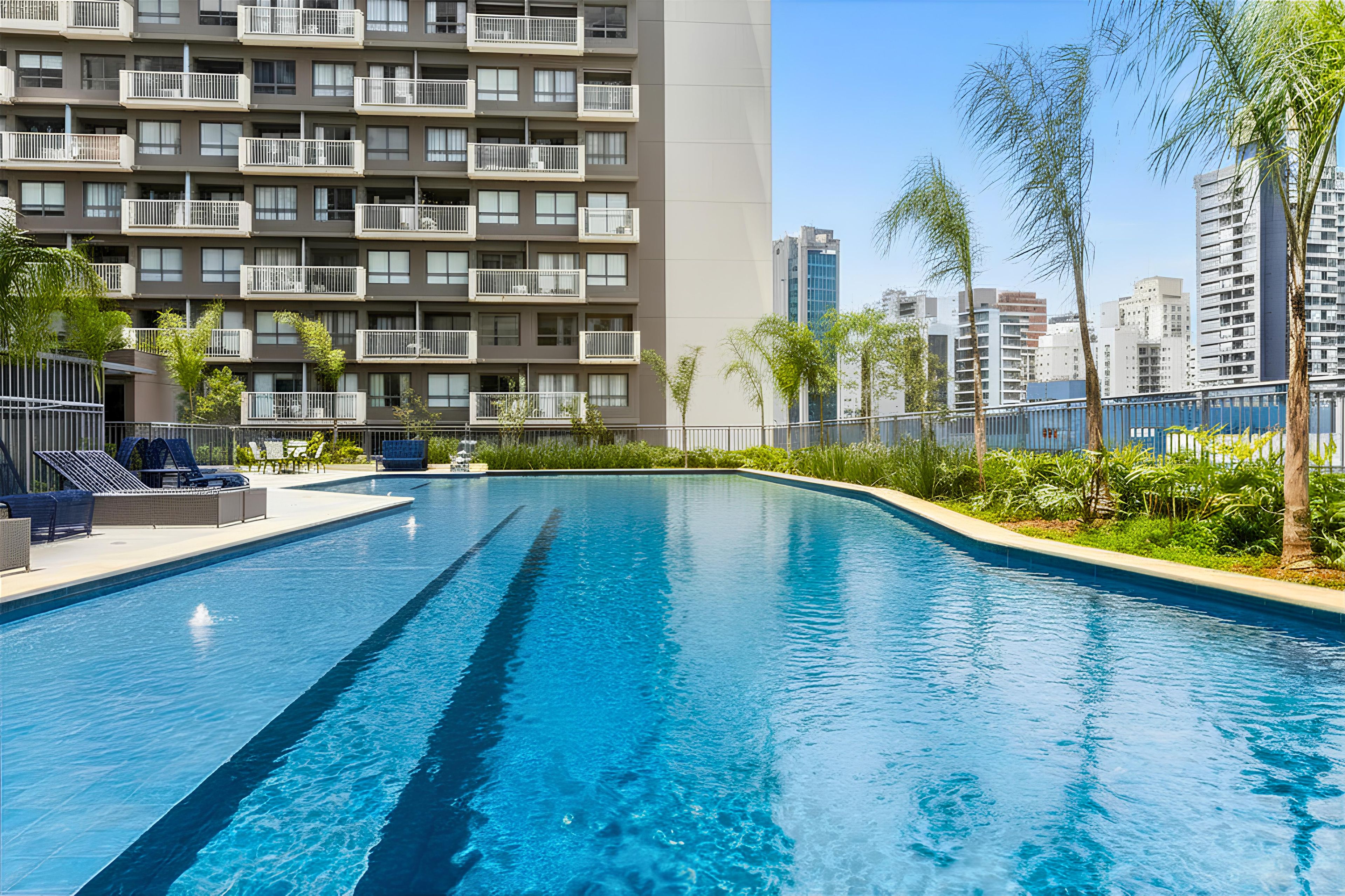 A swimming pool with a clear blue water surface, surrounded by a low fence and lush greenery.