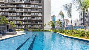 A swimming pool with lounge chairs and a high-rise building in the background.