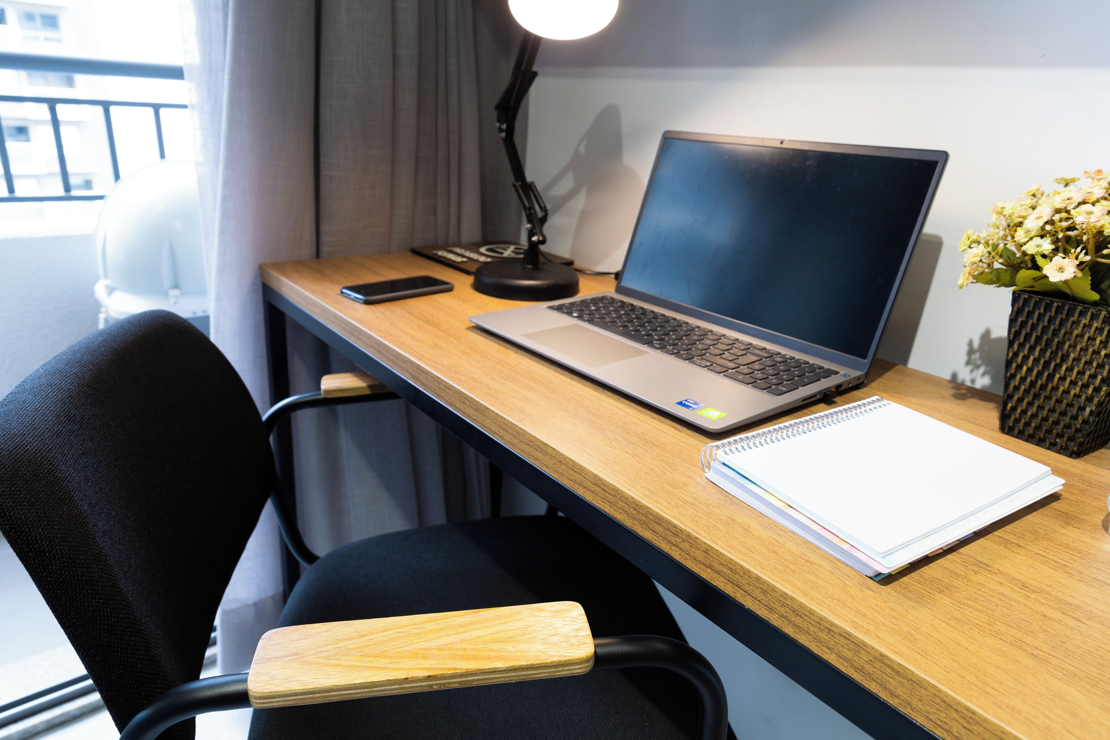 A desk with a laptop, a smartphone, a notebook, and a lamp.