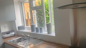Cocina compacta con lavadora integrada, pileta de acero inoxidable y ventana con vista a un muro de ladrillo.