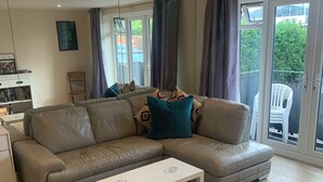 Una sala moderna con un sofá seccional color beige, una mesa de centro blanca y un ventanal de vidrio que da a un balcón.