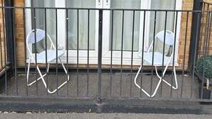 Un balcón con dos sillas plegables blancas y una barandilla de metal.