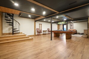 Ein geräumiger Raum mit einer Holztreppe, einem Billardtisch und einem Buntglasfenster.