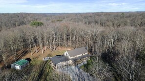 A large house surrounded by dense forest, with a smaller building to the left. - Brawny Woods | Hocking Hills, Hot Tub, Fireplace (South Bloomingville)