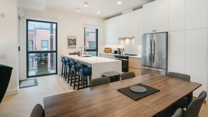 A modern kitchen with a central island, bar stools, and a dining area with a wooden table and chairs. - The Luxury Basecamp in Mackenzie Village (Revelstoke)