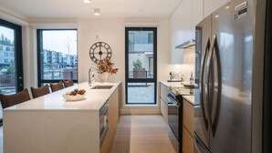 A modern kitchen with a central island, stainless steel appliances, and large windows offering city views. - The Big Lohbow - Ski Haus in Mackenzie Village (Revelstoke)