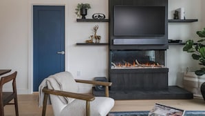 A living room with a blue door, a fireplace, a TV, and a chair. - The Big Lohbow - Ski Haus in Mackenzie Village (Revelstoke)