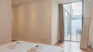 Moderni hotellihuone, jossa on suuri sänky, näkymä ulos liukuovista, ja pieni parveke, jossa on tuoli.