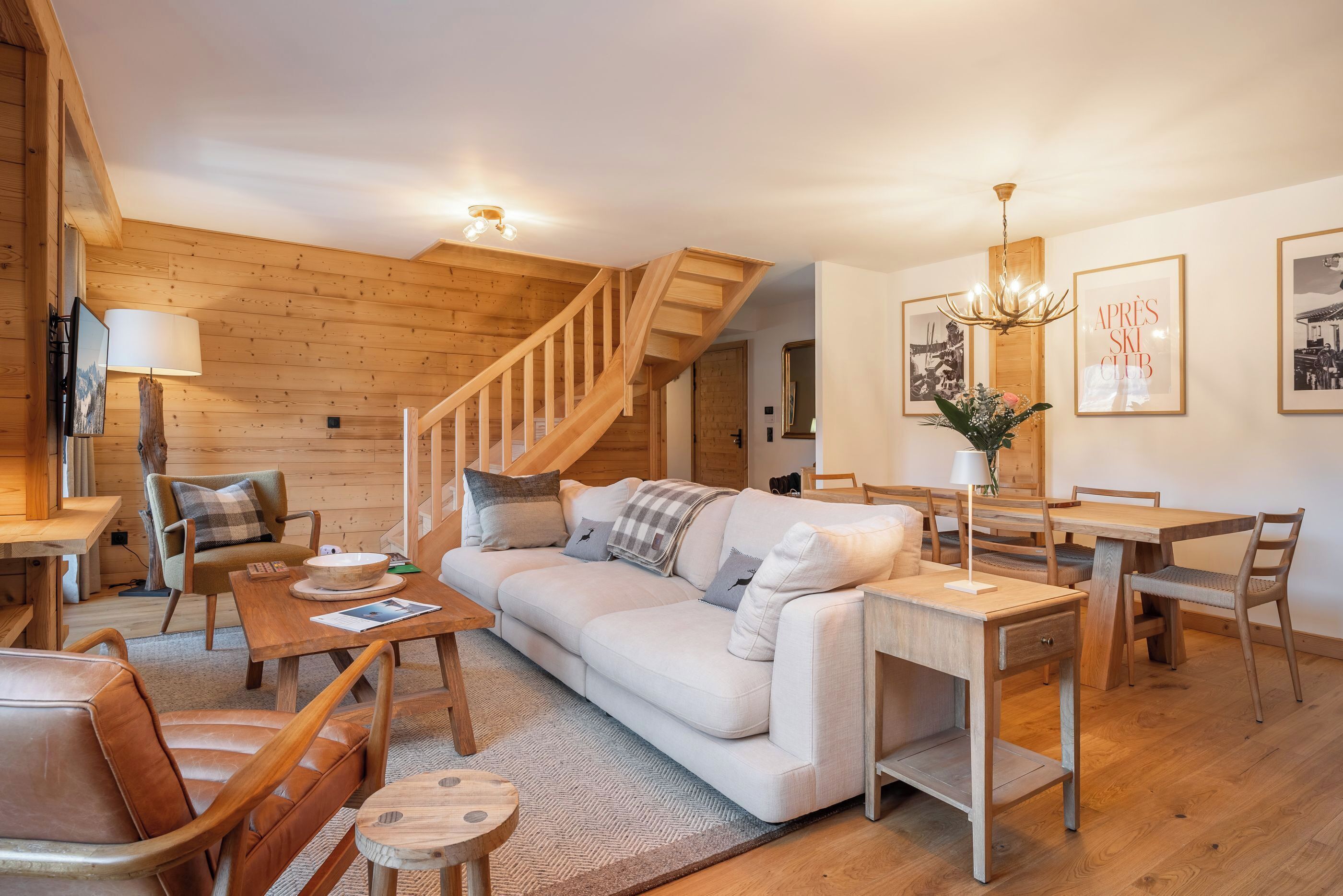 Un salon chaleureux avec un escalier en bois, un canapé, une table à manger et un lustre.