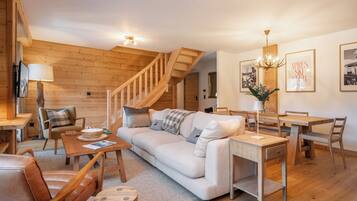 Un salon chaleureux avec un escalier en bois, un canapé, une table à manger et un lustre.