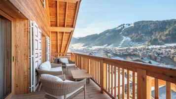 Une terrasse en bois, meublée de meubles en osier, offrant une vue sur la ville et les montagnes.