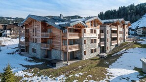A multi-story wooden building with balconies, stone accents, and a ski slope in the background. - Kandahar – Warm Alpine Retreat in Les Gets (Les Gets)