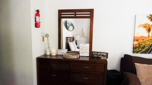 A wooden dresser with drawers, a mirror, a fire extinguisher, a framed picture, and a small table with a vase and a candle. - Feel safe and rest in our cozy 1-bedroom studio with AC (Manatí)