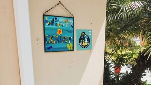 A blue plastic chair outside a building, a wall with a sign, and a potted plant. - Feel safe and rest in our cozy 1-bedroom studio with AC (Manatí)