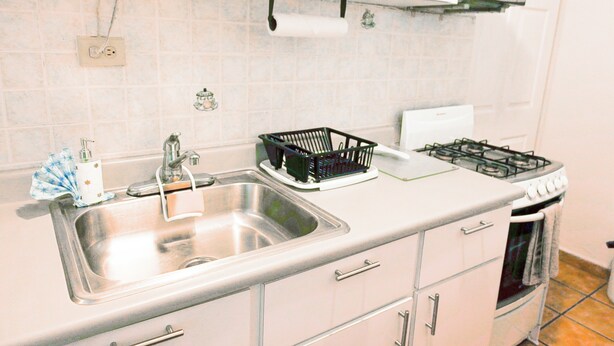 A kitchen with a stainless steel sink, a gas stove, and white cabinets. - Feel safe and rest in our cozy 1-bedroom studio with AC (Manatí)