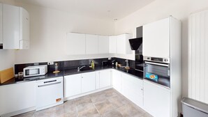 Une cuisine moderne avec des meubles blancs, un plan de travail noir, un four à micro-ondes, un grille-pain, un évier et une cuisinière.