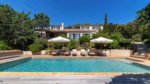 A swimming pool with lounge chairs and umbrellas, surrounded by a wooden deck and lush greenery. - Magnificent villa with sea view, swimming pool, air conditioning, excellent location (La Croix-Valmer)