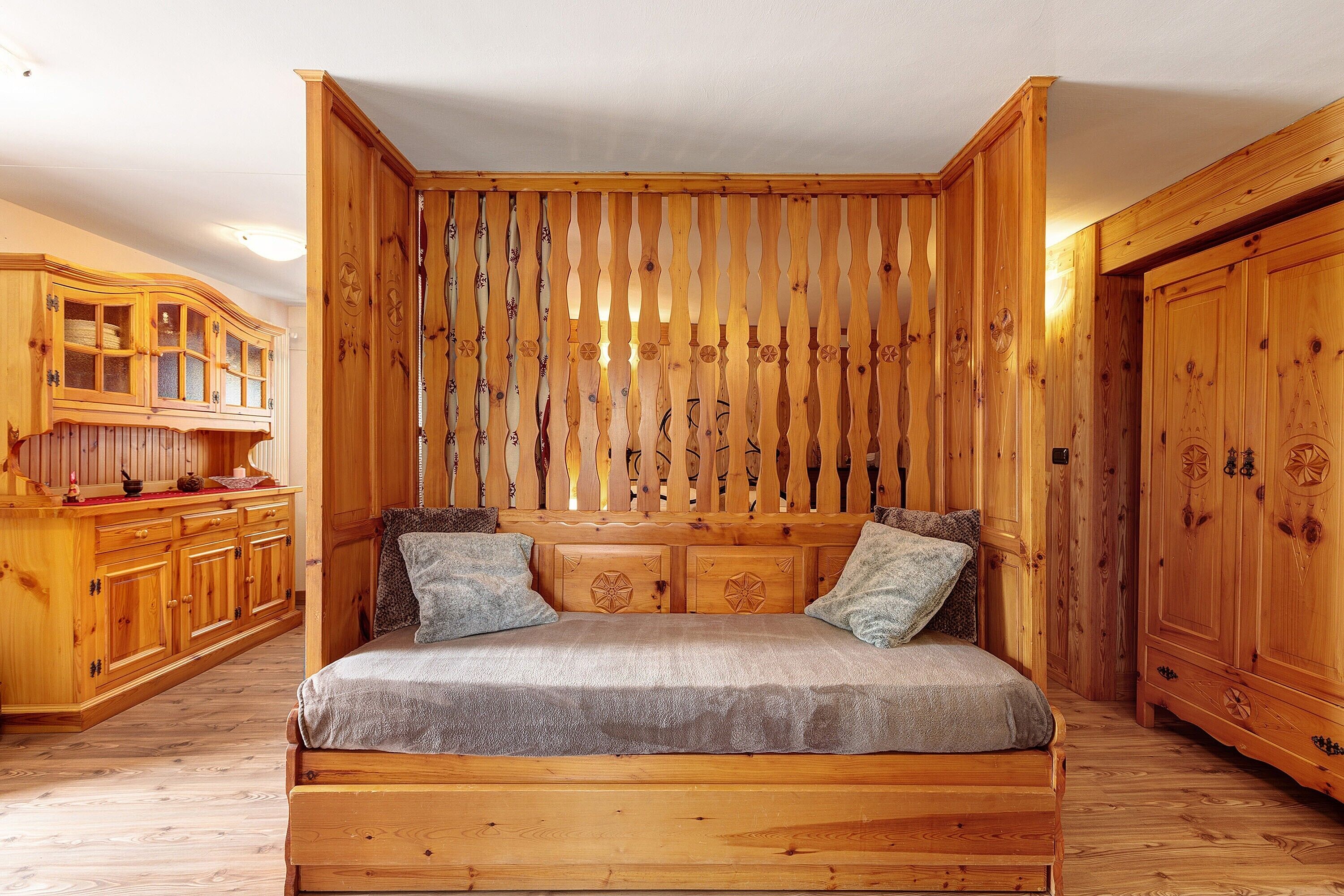 A wooden room with a bed, wooden cabinets, and a slatted wall.