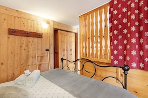 Une pièce en bois avec un lit, un porte-manteau en bois et une fenêtre ornée d’un rideau rouge.